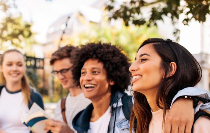 Quatro jovens, duas mulheres e dois homens, caminham juntos enquanto riem e conversam.