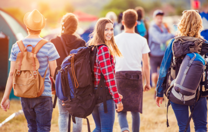 adolescentes felizes andando em direção a um acampamento com a jovem no meio olhando para trás e sorrindo para a câmera